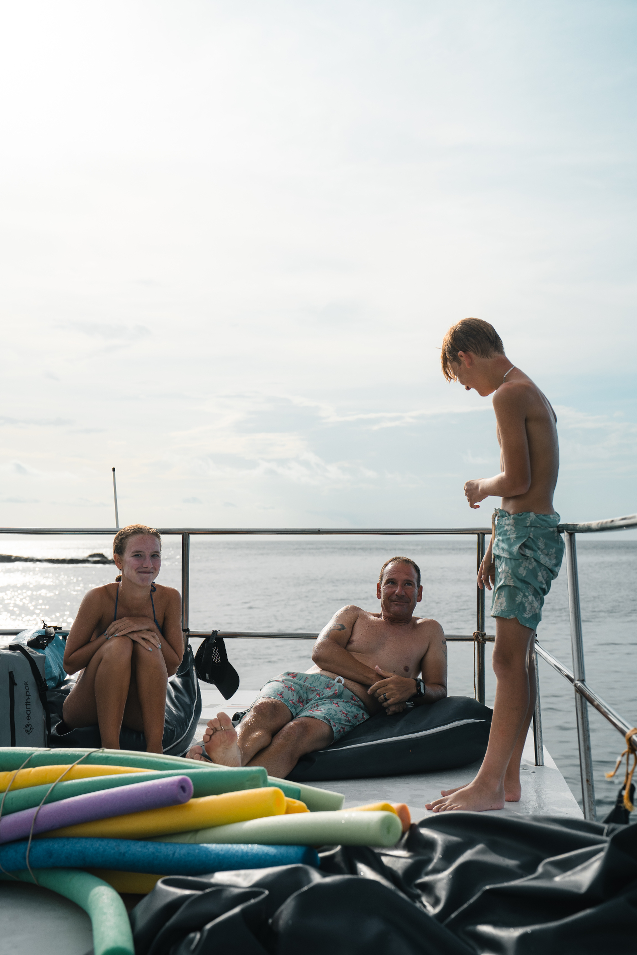 Family relaxing on the Pacific Lounge catamaran deck with pool noodles and ocean views